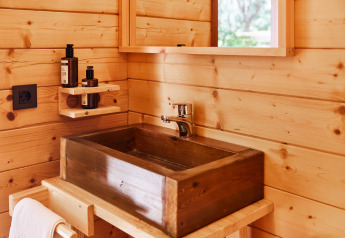 Naturinspireret badeværelse med trævask og vægmonteret hylde med toiletartikler på et glampingsted.
