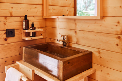 Baño rústico con lavabo de madera y estante con productos de tocador, propio de un alojamiento glamping.