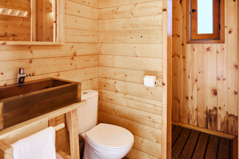 Salle de bain d’un hébergement glamping avec murs en bois, toilettes, lavabo en bois et petite fenêtre.