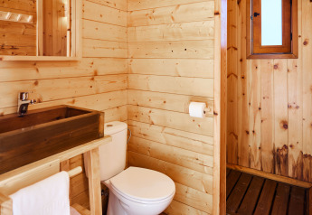 Badezimmer einer Glamping-Unterkunft mit Holzwänden, WC, Holzwaschbecken und kleinem Fenster.