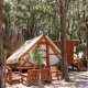 Safari-Zelt Tamaral bei TAIGA Tarifa in Spanien, umgeben von Pinienbäumen und Holzsitzgelegenheiten.