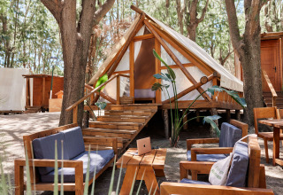Safari tent Tamaral Tent bij TAIGA Tarifa in Spanje, met buitenzitje en houten meubels onder de bomen.
