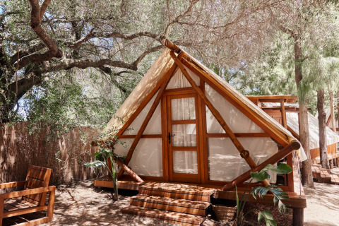 Safari tent Tamaral Tent bij TAIGA Tarifa in Spanje, tussen bomen geplaatst met houten zitmeubilair op het terras.