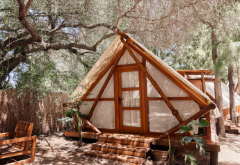 Tenda safari Tamaral Tent al TAIGA Tarifa in Spagna, immersa tra alberi e arredamento in legno su una veranda ombreggiata.