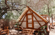 Tamaral Tent at TAIGA Tarifa in Spain, a safari tent set among trees with wooden furniture on a shaded deck.
