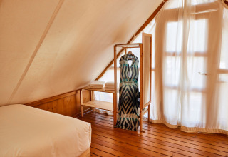 Interieur van Tamaral safaritent bij TAIGA Tarifa in Spanje, met houten vloer en rek met kleding aan raam.