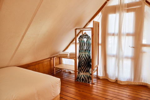 Interieur van Tamaral safaritent bij TAIGA Tarifa in Spanje, met houten vloer en rek met kleding aan raam.