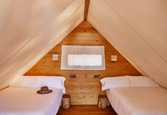 Interieur van de Tamaral safari tent bij TAIGA Tarifa in Spanje, met twee bedden en houten muren.