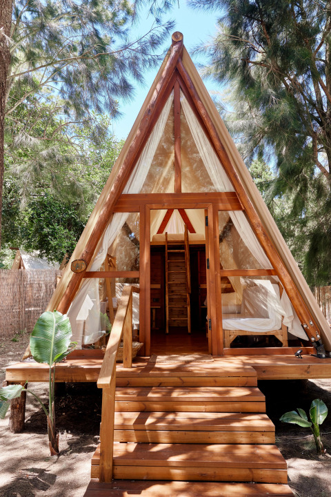 A-frame houten safaritent met open deuren en natuurlijk licht bij TAIGA Tarifa, Spanje, omringd door bos.