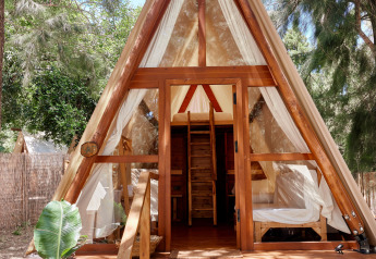 Tente safari en bois en forme de A à TAIGA Tarifa, Espagne, avec portes ouvertes, baignée de lumière et forêt alentour.