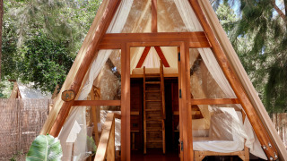 Tente safari en bois en forme de A à TAIGA Tarifa, Espagne, avec portes ouvertes, baignée de lumière et forêt alentour.
