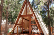 Sauceda Tent im TAIGA Tarifa, Spanien – A-förmiges Safarizelt mit Holzterrasse im Schatten hoher Bäume.
