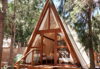 Sauceda Tent at TAIGA Tarifa, Spain, an inviting A-frame safari tent in a wooded area with wooden steps.