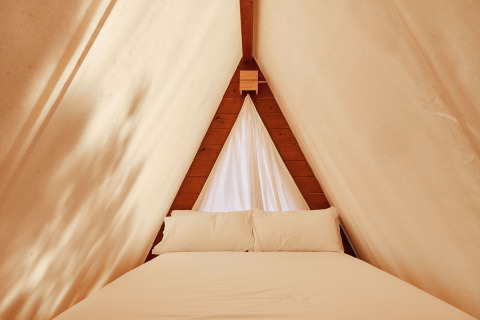 Innenansicht des Sauceda Zeltes bei TAIGA Tarifa in Spanien, mit gemütlichem Bett und hellen Vorhängen.