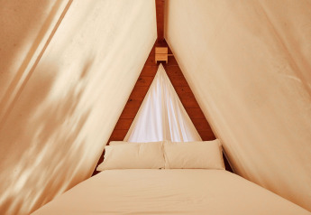 Vue intérieure de la tente Sauceda au TAIGA Tarifa en Espagne, avec lit confortable et rideaux clairs.