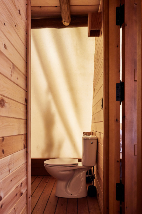 Baño con inodoro en la carpa Sauceda de TAIGA Tarifa, España, con paredes de madera e iluminación natural.