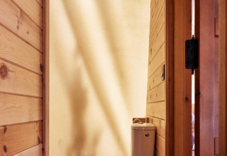 Baño con inodoro en la carpa Sauceda de TAIGA Tarifa, España, con paredes de madera e iluminación natural.