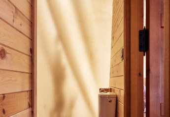 Baño con inodoro en la carpa Sauceda de TAIGA Tarifa, España, con paredes de madera e iluminación natural.