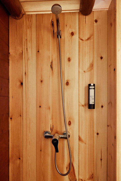 Ducha con paredes de madera en la tienda Sauceda de TAIGA Tarifa, España, con grifería moderna.
