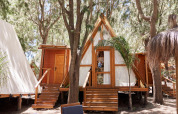 Zona de estar exterior frente a la tienda Algaida en TAIGA Tarifa, España, con bosque y cabañas alrededor.