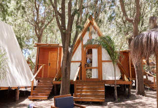 Zona de estar exterior frente a la tienda Algaida en TAIGA Tarifa, España, con bosque y cabañas alrededor.