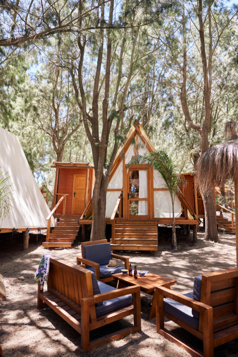 Zona de estar exterior frente a la tienda Algaida en TAIGA Tarifa, España, con bosque y cabañas alrededor.