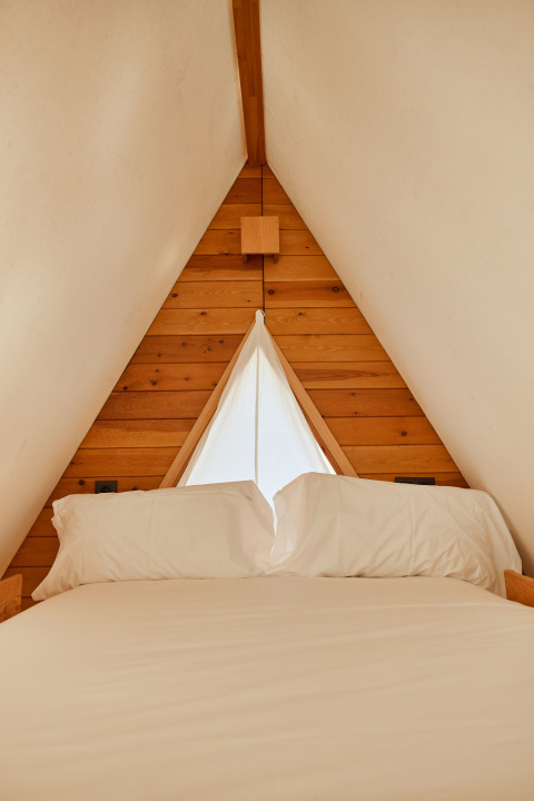 Interior de la tienda Algaida en TAIGA Tarifa, España, con cama acogedora y pared triangular de madera.