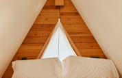 Interior de la tienda Algaida en TAIGA Tarifa, España, con cama acogedora y pared triangular de madera.