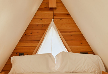 Interno della tenda Algaida al TAIGA Tarifa, Spagna, con letto accogliente e parete di legno triangolare.