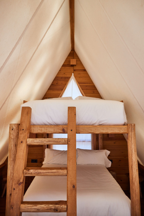 Interior de la tienda safari Algaida Tent en TAIGA Tarifa, España, con literas de madera y paredes claras.