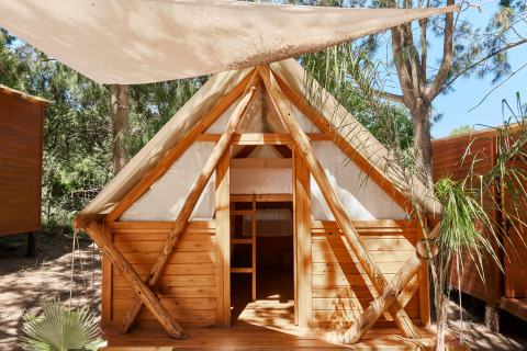 Janda Tent blokhut bij TAIGA Tarifa in Spanje, met stapelbedden en canvas dak, omgeven door bomen.