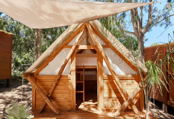 Janda Tent blokhut bij TAIGA Tarifa in Spanje, met stapelbedden en canvas dak, omgeven door bomen.