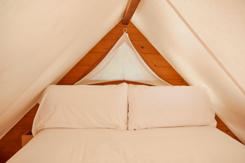 Interno della tenda Janda al TAIGA Tarifa in Spagna, con letto accogliente e pareti in legno chiaro.
