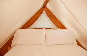 Interior de la tienda Janda en TAIGA Tarifa, España, con una cama acogedora y paredes de madera clara.