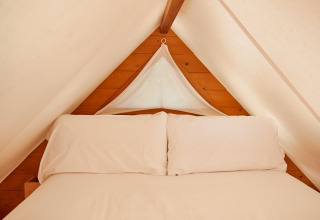 Interieur van de Janda-tent bij TAIGA Tarifa in Spanje met een knus bed en lichte houten wanden.