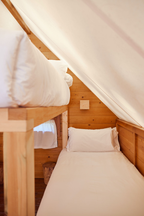 Interieur van de Janda Tent bij TAIGA Tarifa, Spanje, met houten wanden en twee eenpersoonsbedden onder een schuin dak.
