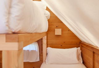 Interior de la Janda Tent en TAIGA Tarifa, España, con paredes de madera y dos camas individuales bajo techo inclinado.