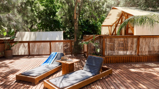 Outdoor deck with sun loungers and a luxury glamping tent at La Cala, TAIGA Tarifa, surrounded by greenery.