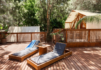Terrasse en bois avec transats et tente glamping de luxe à La Cala, TAIGA Tarifa, entourée de verdure.