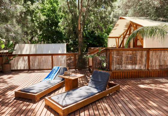 Outdoor deck with sun loungers and a luxury glamping tent at La Cala, TAIGA Tarifa, surrounded by greenery.