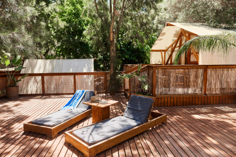 Terrasse en bois avec transats et tente glamping de luxe à La Cala, TAIGA Tarifa, entourée de verdure.