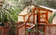 Glamping Luxury Tent La Cala at TAIGA Tarifa, Spain, featuring a wooden terrace surrounded by lush greenery.