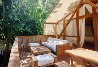 Udendørs terrasse med træmøbler og puder foran et glamping-luksustelt ved TAIGA Tarifa, Spanien.