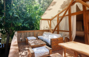 Terraza de madera con sofás y cojines frente a una tienda glamping de lujo en TAIGA Tarifa, España.