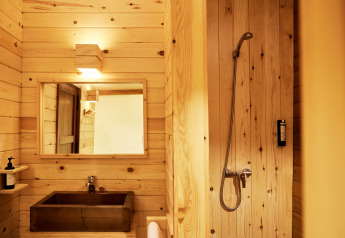 Baño de madera luminoso con ducha y lavabo en Glamping Luxury Tent La Cala, TAIGA Tarifa, España.