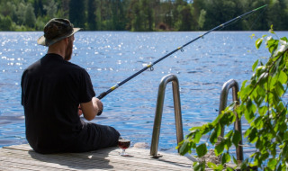 Mann angelt entspannt auf einem Steg an einem See in einem Ferienpark mit Glamping-Unterkünften.