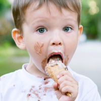 Young boy eating an ice cream cone with messy face and shirt, taken at a glamping holiday park.