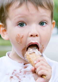 Kleine jongen eet een ijsje, met ijs op zijn gezicht en t-shirt, op een glamping vakantiepark.