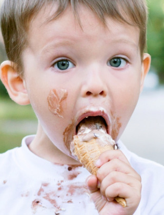 Kleiner Junge genießt ein Eis mit Eis im Gesicht und auf dem Shirt, in einem Glamping-Ferienpark.