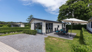 Vue sur le chalet Velthorst avec jardin, terrasse et parasol à EuroParcs Parc du Soleil aux Pays-Bas.